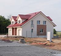 A family house in Andovce with a red roof surrounded by trees and a landscaped driveway.