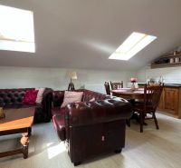 Attic interior with a leather sofa set, wood-patterned flooring, and a dining area.