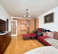 Living room in a two-room apartment with a red sofa, TV, and wooden decor flooring.