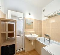 A bathroom with a bathtub and a sink in a 2-room apartment, light tiles, shelves.
