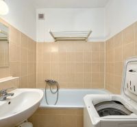 A bathroom with a washing machine and a bathtub in a 2-room apartment with beige tiles.