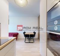 A kitchen in a 2-room apartment with ovens, a dining table, and a floor with a wooden decor.