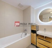 A bathroom in a 2-room apartment with a bathtub, a sink, and a lighted mirror.