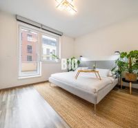A bright bedroom in a three-room apartment with a bed, plants, and a wooden decor floor.