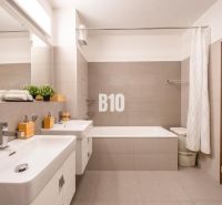 A bathroom in a 3-room apartment with a bathtub, two sinks, and neutral tiles.