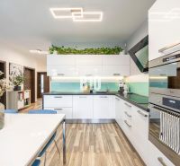 A kitchen with light furniture, modern appliances, and a floor with a wooden decor in a 3-room apartment.