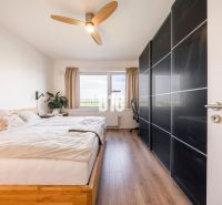 A bright bedroom with a large bed, wood-patterned flooring, and a wardrobe.