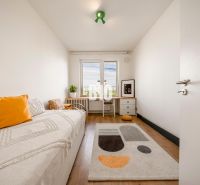 A room in a 3-room apartment with a bed, a table, a floor with a wooden decor, and a colorful carpet.