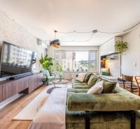 Living room in a 3-room apartment with a comfortable green sofa, a large television, and plants.