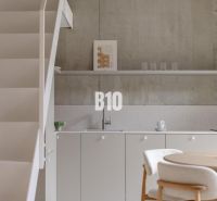 The kitchen part of a 2-room apartment with a minimalist design and a concrete wall.