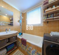 A bathroom in a 3-room apartment with a bathtub, washing machine, sink, and storage shelves.