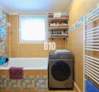 A bathroom in a 3-room apartment with a washing machine, a bathtub, and orange tiles.