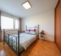 A bedroom with a bed, a cabinet, and a wooden decor floor in a three-room apartment.