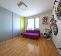 A room with a purple sofa, a wooden-patterned floor, and a shelf with medals in a three-room apartment.