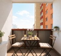 A balcony in a 3-room apartment in Bratislava V with seating, flowers, and a view of the sky.