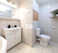 Bathroom with a bathtub, sink, mirror, toilet, and decorative shelves in a 3-room apartment.