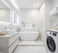 Stylish bathroom with a bathtub and washing machine in a 3-room apartment, white marble tiles.