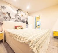 A bedroom in a 3-room apartment with floral wallpaper, yellow details, and a floor with a wooden decor.