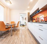 A kitchen in a 3-room apartment with orange chairs, a wooden decor floor, and colorful tiles.