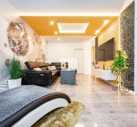 Interior of a 3-room apartment with a sofa, large television, wall decor, and wood-patterned flooring.