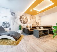 Living room of a three-room apartment with a comfortable sofa and a wooden-patterned floor.