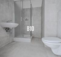 Bathroom with a shower and light tiles in a studio apartment.
