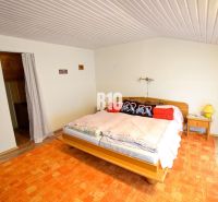 A bedroom in a cottage with a bed, decorative pillows, and an orange carpet.