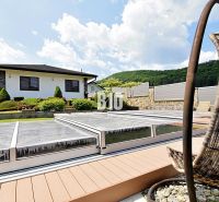 A family house in Súľov-Hradná with a covered swimming pool and a landscaped garden on a sunny terrace.