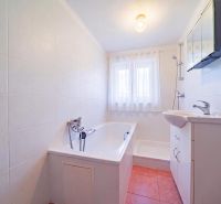 A bathroom in a family house with a shower, bathtub, sink, and a window with white curtains.