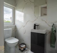 Bathroom with a mirror, sink, and toilet in a 4-room apartment, with marble design tiles.