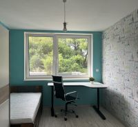 A room in a family house with a desk, a bed, and a floor with a wooden decor.