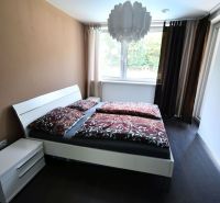 A bedroom with a light wall, a bed, and a wooden decor floor in a family house.