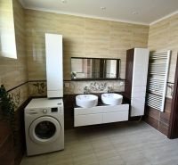 A bathroom with two sinks, a washing machine, and cabinets in a family house.