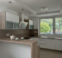 A kitchen in a family house with wooden decor, a large window, and appliances.