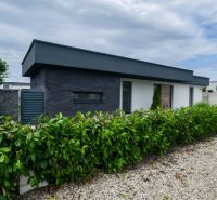 A family house in Košúty with stone cladding, a landscaped garden, and a hedge.