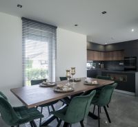 Dining room in a family house with a wooden table, green chairs, and a black kitchen.