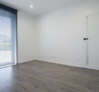 A room with a wooden decor floor, white walls, and vertical blinds in a family house.