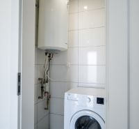 Washing machine and boiler in the bathroom of a family house, tiled with white tiles.