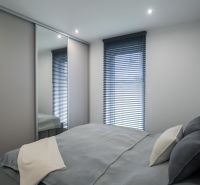 A bedroom in a family house with a large built-in wardrobe, a bed, and blinds.