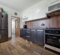 A kitchen in a 3-room apartment with a wooden decor floor and dark furniture.