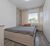 A bedroom with a bed, cabinet, window, and wooden decor flooring in a 3-room apartment.