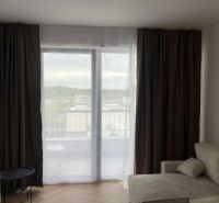 Living room in a two-room apartment with a wooden decor floor and curtains.