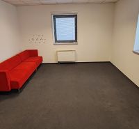 A red sofa in an office with a window and a radiator, dark decor flooring.