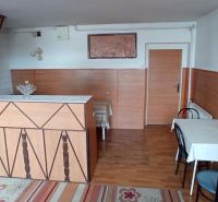 Interior of a building with a kitchen counter, tables, and a wood-patterned floor.