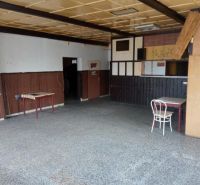 The building has old tables, a chair, wall paneling, and a stone floor.