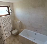 A bathroom in a family house with a bathtub, tiles, and a window for natural light.