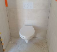 A toilet in a family house with ceramic tiles and a floor with a stoneware design.