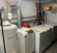 A boiler room in a family house with a boiler and a furnace, white walls, a basket on the piping.