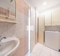 A bathroom in a 2-room apartment with a washing machine, mirror, and cabinets for storage.