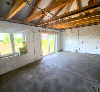 The interior of a family house with an unfinished concrete floor and a wooden beam ceiling.
